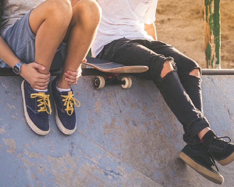 Close up of two young boys sitting on half pipe ramp, after nice tricks and jumps at the skatepark. Trendy teenagers enjoying free time at the skate park. Youth, togetherness and friendship concept.